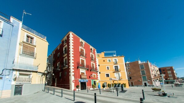 A row of colorful buildings with balconies, a clear blue sky, and a pedestrian area with bollards. - HAPPY - ESTUDIO VISTAS A CALLE (Villajoyosa)