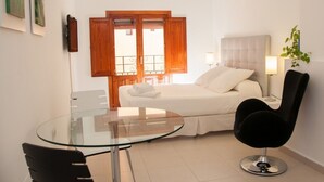 A modern bedroom with a bed, bedside table, lamp, and a glass table with a chair. - HAPPY  - ESTUDIO VISTAS A CALLE (Villajoyosa)