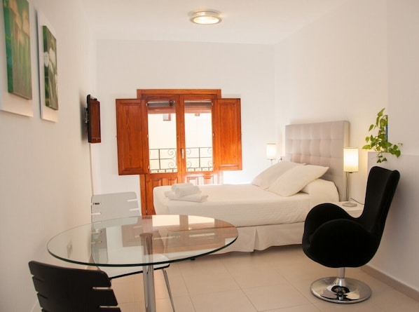 A modern bedroom with a bed, bedside table, lamp, and a glass table with a chair. - HAPPY - ESTUDIO VISTAS A CALLE (Villajoyosa)