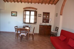 Un coin repas avec une table et des chaises en bois, une fenêtre donnant sur un beau paysage, un canapé rouge et un meuble contenant des ustensiles de cuisine.