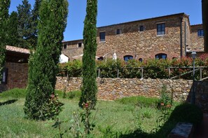 Un bâtiment en pierre, doté d’un toit en tuiles, entouré de verdure et délimité par un mur de pierre.