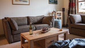 A living room with a brown sofa, a wooden coffee table, and a bottle of wine. - Highland Holiday Homes - Tulloch Ard (Aviemore)