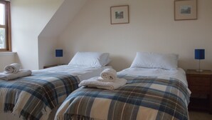A bedroom with two beds, each with a blue and white plaid blanket and white pillows. There are two framed pictures on the wall, a window with curtains, and a nightstand with a lamp. - Highland Holiday Homes - Tulloch Ard (Aviemore)