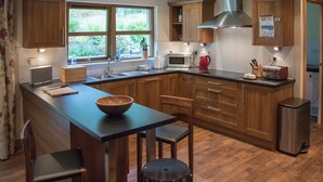 A modern kitchen with wooden cabinets, a central island with stools, a microwave, a toaster, and a stainless steel refrigerator. - Highland Holiday Homes - Tulloch Ard (Aviemore)