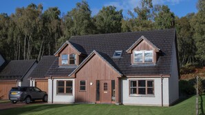 A two-story house with a sloped roof, a garage, and a driveway. - Highland Holiday Homes - Tulloch Ard (Aviemore)