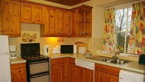 Una cocina con armarios de madera, estufa, lavavajillas y una ventana con cortinas.