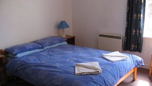 Una cama individual con ropa de cama azul, una lámpara de noche y un radiador.