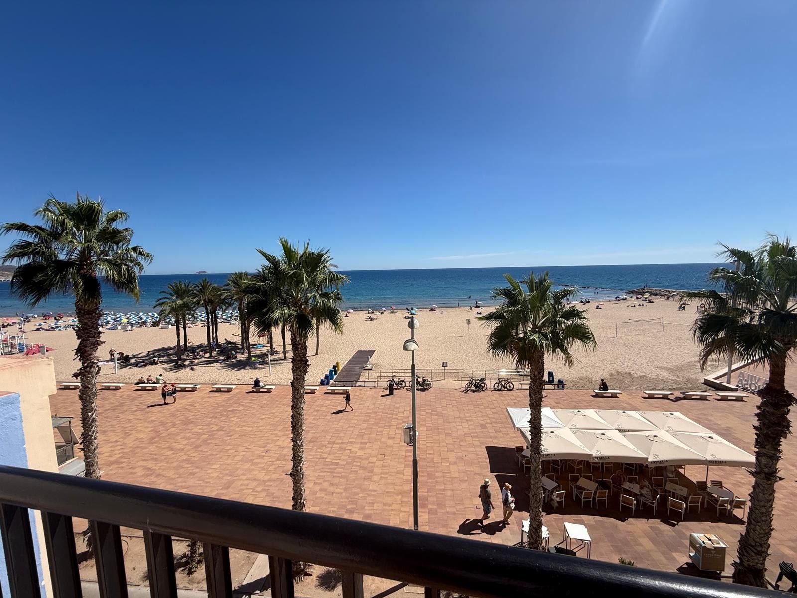 Een uitzicht op het strand met palmbomen, zand en een gebouw met terras.