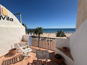 Een balkon met uitzicht op een strand, een stoel, een tafel en een plant in pot.