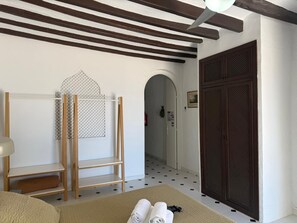 Een kamer met een bed, een houten plank, een decoratieve wandhanger, een deur met gaas en een betegelde vloer.
