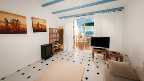 Un soggiorno con TV, divano e vista sul mare tramite una porta vetrata.