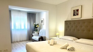 Hotelkamer met een groot bed, een stoel, een nachtkastje met een lamp en een schilderij aan de muur.