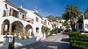 A narrow street lined with white buildings featuring balconies and arched doorways.