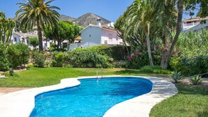 A swimming pool with a curved edge, surrounded by lush greenery and palm trees.