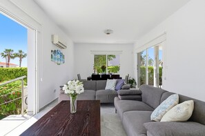 Ein modernes Wohnzimmer mit grauem Sofa, einem Couchtisch und einem Essbereich mit Tisch für zwei Personen.