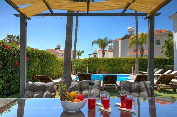 Ein Poolbereich mit Liegestühlen, einem Tisch mit Früchten und Getränken und freiem Blick auf den Pool.