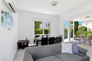 Un salon moderne avec un canapé gris, une table à manger dressée pour quatre personnes et une grande porte-fenêtre coulissante donnant sur un espace extérieur.