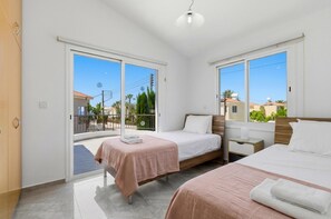 A bedroom with two beds, a balcony, and a view of the sea.