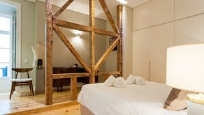 Ein Schlafzimmer mit Holzbalkendecke, einem Bett mit weißen Leinentüchern, einem Sessel und einem Schreibtisch.