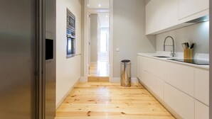 Eine schmale Küche mit Holzboden, einem Edelstahlkühlschrank, einer Mikrowelle und einem Waschbecken mit Wasserhahn.