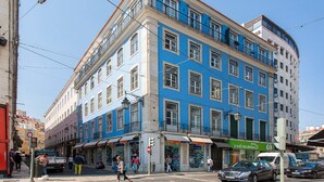 Ein mehrstöckiges Gebäude mit blauer Fassade, Geschäften im Erdgeschoss und einer sichtbaren Straßenecke.