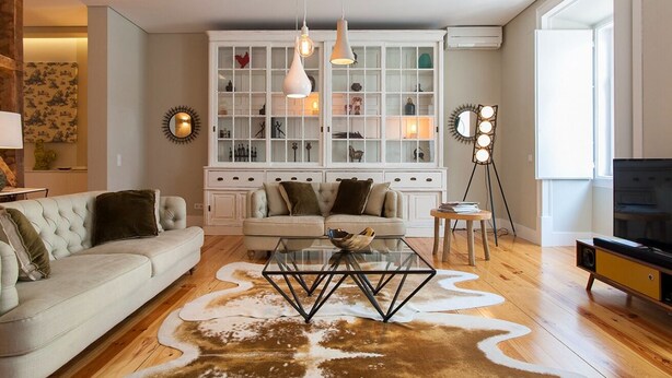 Ein Wohnzimmer mit einer Couch, einem Glastisch, einem Schrank mit Glastüren, Pendelleuchten und einer Stehlampe.