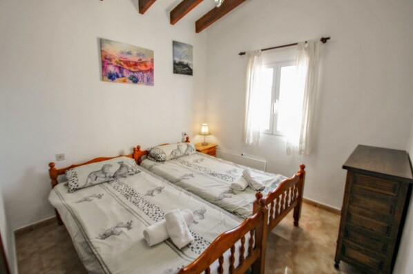 A bedroom with two single beds, a wooden dresser, a nightstand with a lamp, and a window with curtains. - Cometa-86 - Pool, Terrace & Landscape View (Calpe)