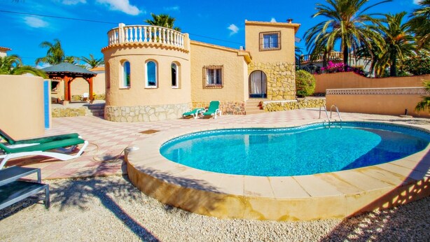 Una piscina con lettini, un edificio in pietra con finestre ad arco e palme.