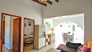 Un'ampia zona giorno con divano, un tavolino in legno e un tavolo da pranzo con sedie. È presente un angolo cottura con pensili e una lampada. L'ambiente ha una disposizione aperta che si affaccia sulla zona pranzo.