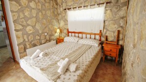 Una camera da letto con parete in pietra, struttura del letto in legno, copripiumino bianco e comodino con lampada.