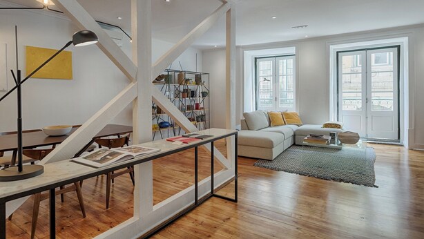 Una sala de estar moderna con una escalera, piso de madera, un sofá con cojines, una mesa de centro y una estantería.