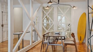 Un comedor moderno con una mesa y sillas de madera, una tabla de surf amarilla apoyada en la pared, y un diseño de ventana geométrico único.