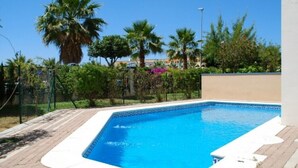 Una piscina rettangolare con bordo bianco, circondata da un vialetto in mattoni e palme.