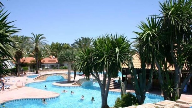 Ein Poolbereich mit mehreren Schwimmbecken, Palmen und einer Rutsche.