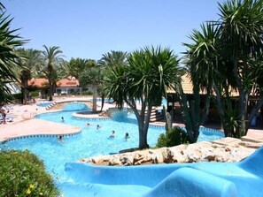 A pool area with multiple swimming pools, palm trees, and a water slide. - Apartment for 4 people in urbanization El Palmar with pool of slides. (Dénia)