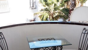 Ein Tisch mit Glasplatte, zwei Stühle, eine weiße Wand und Blick auf Palmen.