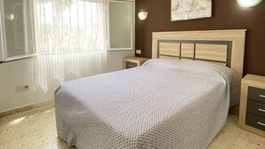 Ein Schlafzimmer mit Bett, Nachttischen, einem Fenster mit Vorhängen und Wandleuchten.