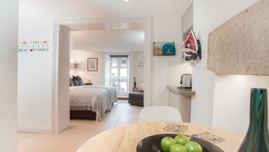 A modern bedroom with a bed, bedside table, and a view into another room. - The Design Studio (Bath)