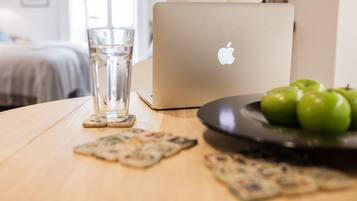 A laptop on a table with a glass of water, a plate of green apples, and some coasters.