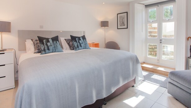 A modern bedroom with a large bed, bedside tables, a lamp, and a view of the outdoors through a door. - The Design Studio (Bath)
