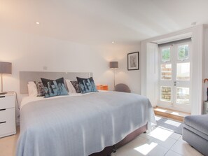 A modern bedroom with a large bed, bedside tables, a lamp, and a view of the outdoors through a door. - The Design Studio (Bath)