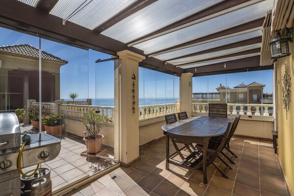 A covered outdoor patio with a grill, dining table, chairs, and potted plants.