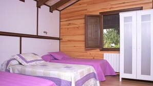 Una habitación con dos camas, paredes de madera, una ventana que da a zonas verdes y un armario blanco.