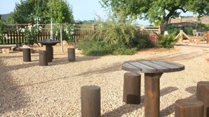 Un parque infantil con una mesa de madera y bancos, rodeado de grava y árboles.