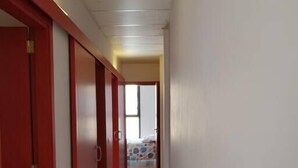 Un couloir avec des portes rouges, un sol carrelé et un lit visible au loin.