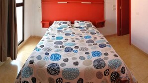 Un lit avec une couvre-lit à motifs, une tête de lit rouge et une fenêtre avec des rideaux.