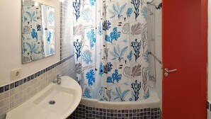 Une salle de bain avec un lavabo blanc, une douche avec un rideau à motifs floraux et une porte rouge.