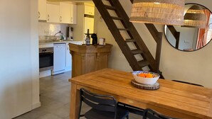 Una cocina con armarios blancos, una isla de madera y una mesa de comedor con sillas. Hay un cuenco de naranjas sobre la mesa.