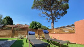 Un patio con dos tumbonas, una valla de madera y un árbol grande.