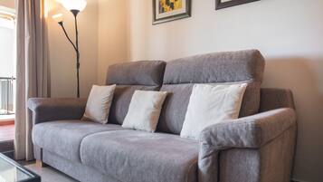 Ein graues Sofa mit mehreren Kissen, einer Stehlampe und zwei gerahmten Kunstwerken an der Wand.